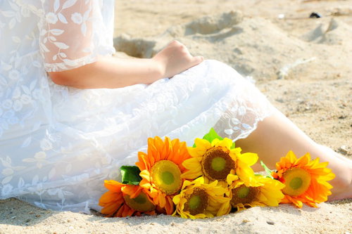 砂浜で花束を抱きしめ想い出に浸る白いドレスの女性