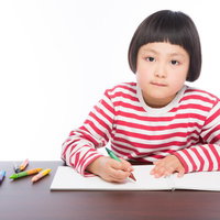 赤と白のボーダーシャツでクレヨンでお絵かきする女の子の写真