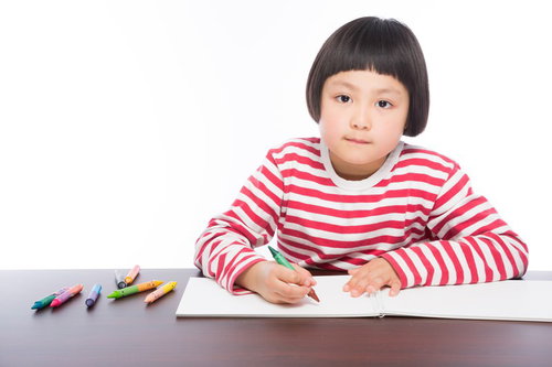 赤と白のボーダーシャツでクレヨンでお絵かきする女の子