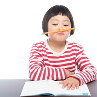 宿題に集中できず鉛筆をくわえて考え込む小学生の写真