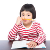宿題に飽きて鉛筆をくわえる小学生の勉強風景の写真
