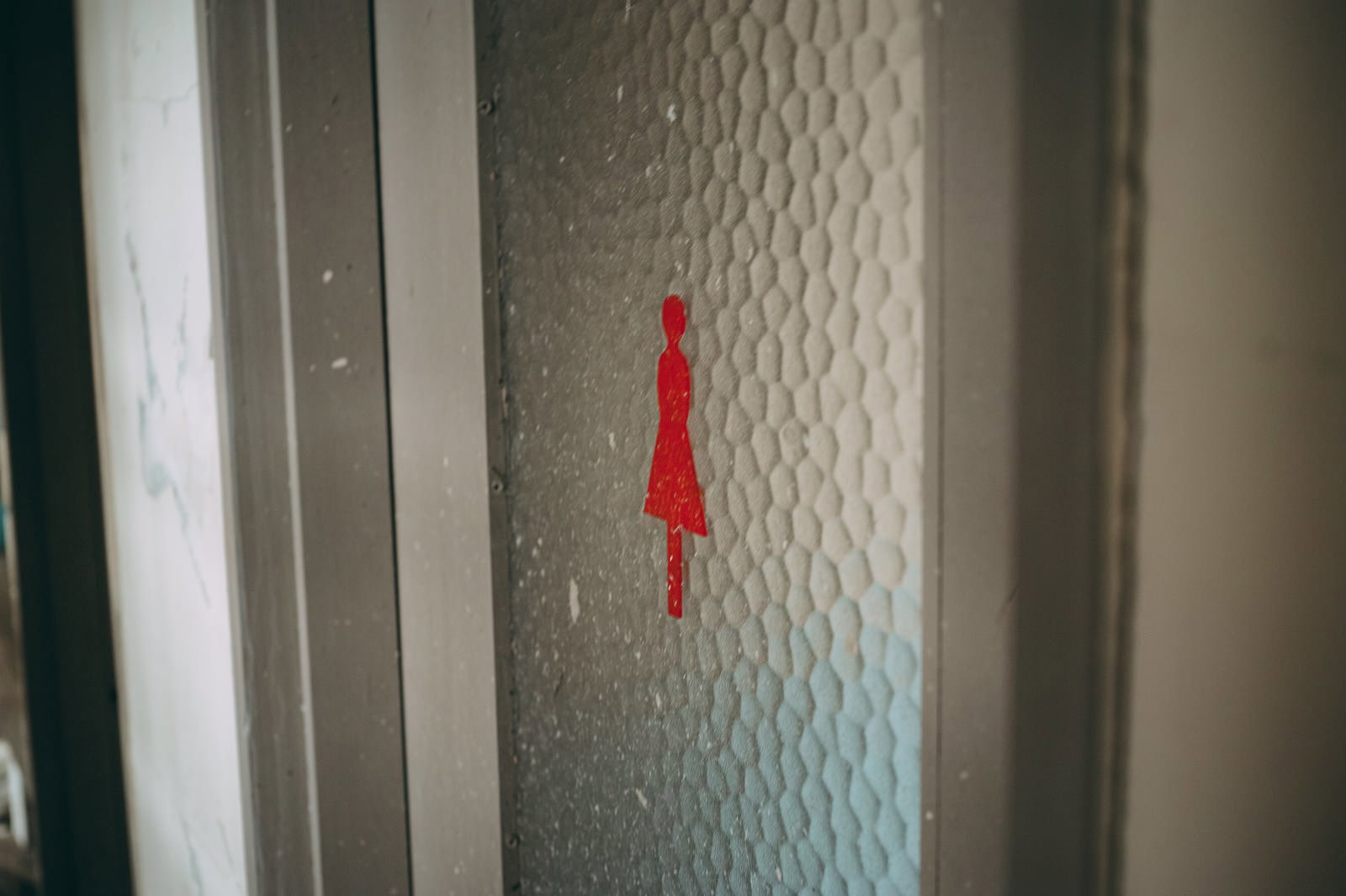 廃墟の女子トイレの扉に赤い女性マークが貼られた室内