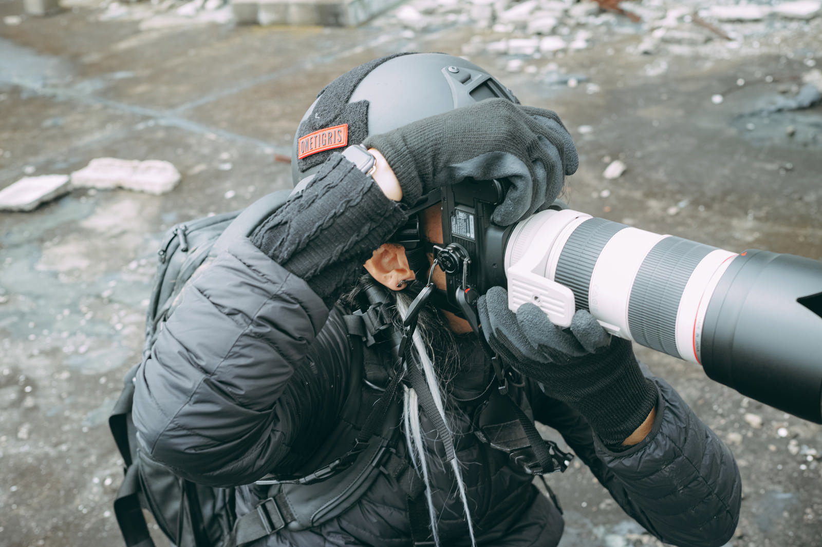 ヘルメットと防護服を着用した男性カメラマンが望遠レンズ付きカメラで撮影している［モデル：YAT］