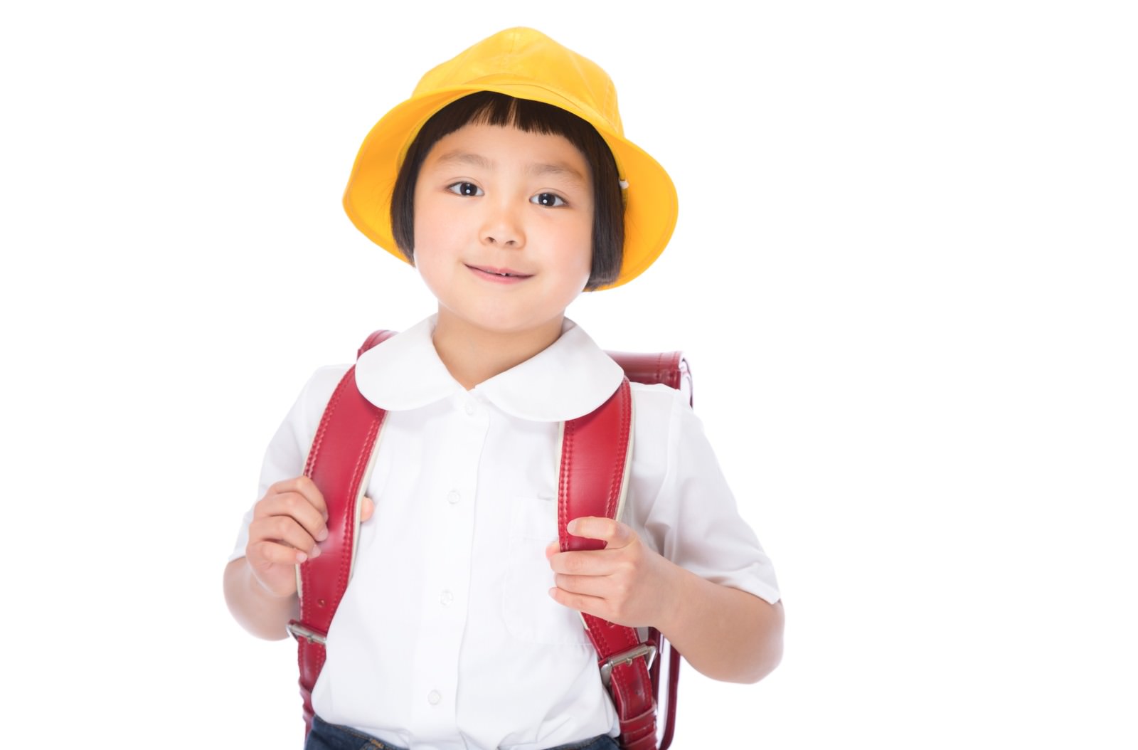 黄色い帽子と赤いランドセルを背負った新一年生の女の子が笑顔で立っている［モデル：ゆうき］