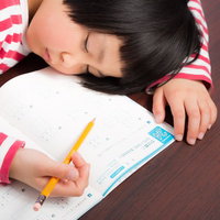 宿題しながらスースーと寝息を立てるおかっぱの女の子の写真