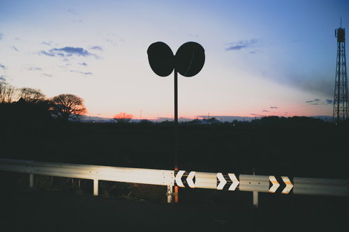 夕焼け空でシルエットになったガードレールに映るヘッドライトの光