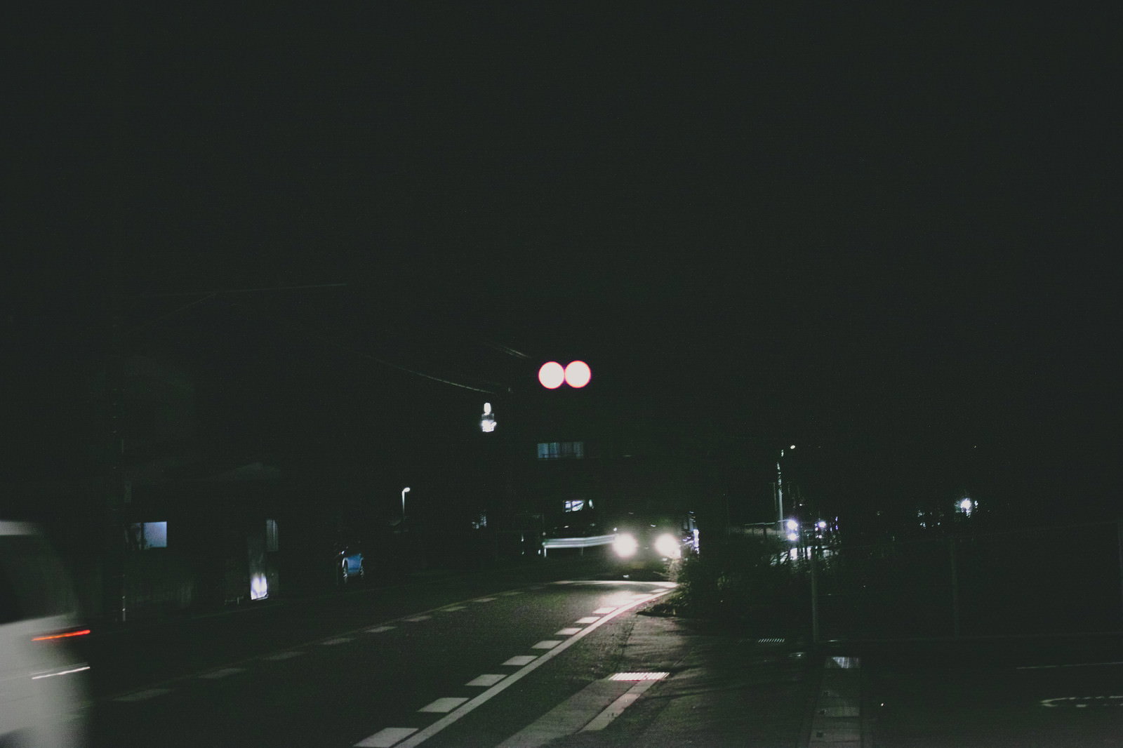 暗い夜道で白く光る車のヘッドライトが車道を照らしている様子