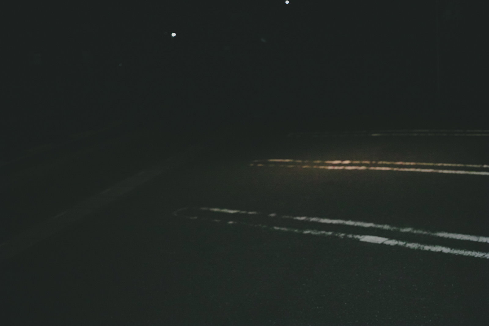 A nighttime scene of a parking lot with spaces marked by white lines in the darkness