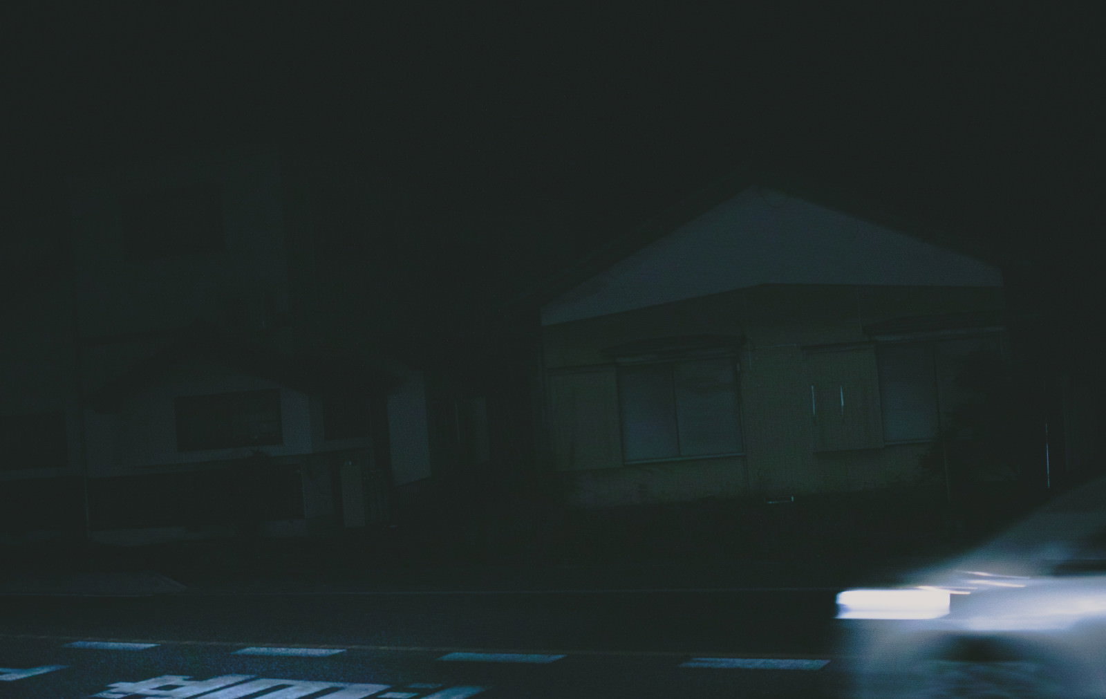 深夜の住宅街で車のヘッドライトが白い光跡を描いている様子
