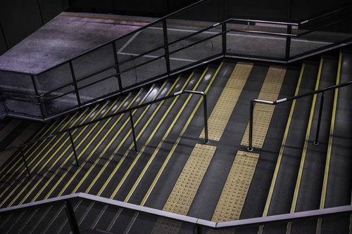 誰もいない夜の駅構内階段、蛍光灯と黄色い安全線が照らす地下通路