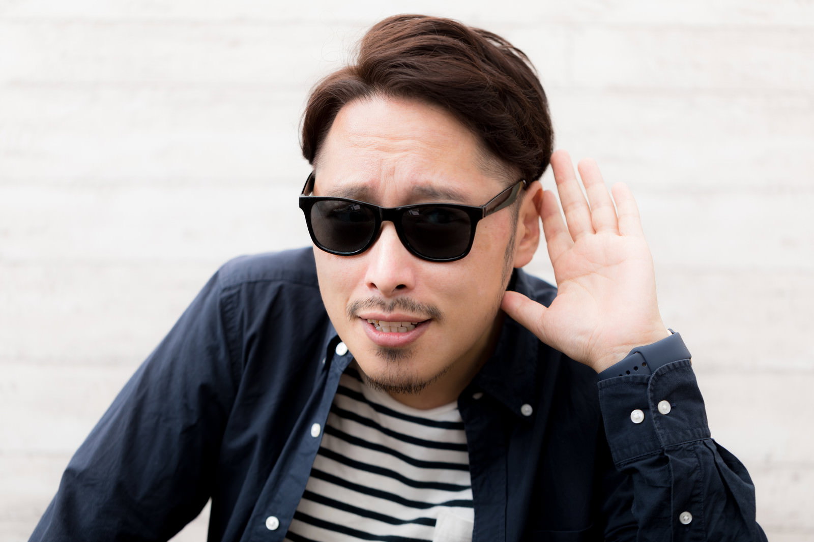 サングラスをかけて手を耳に当てて聞き返すポーズの男性［モデル：ゆうせい］
