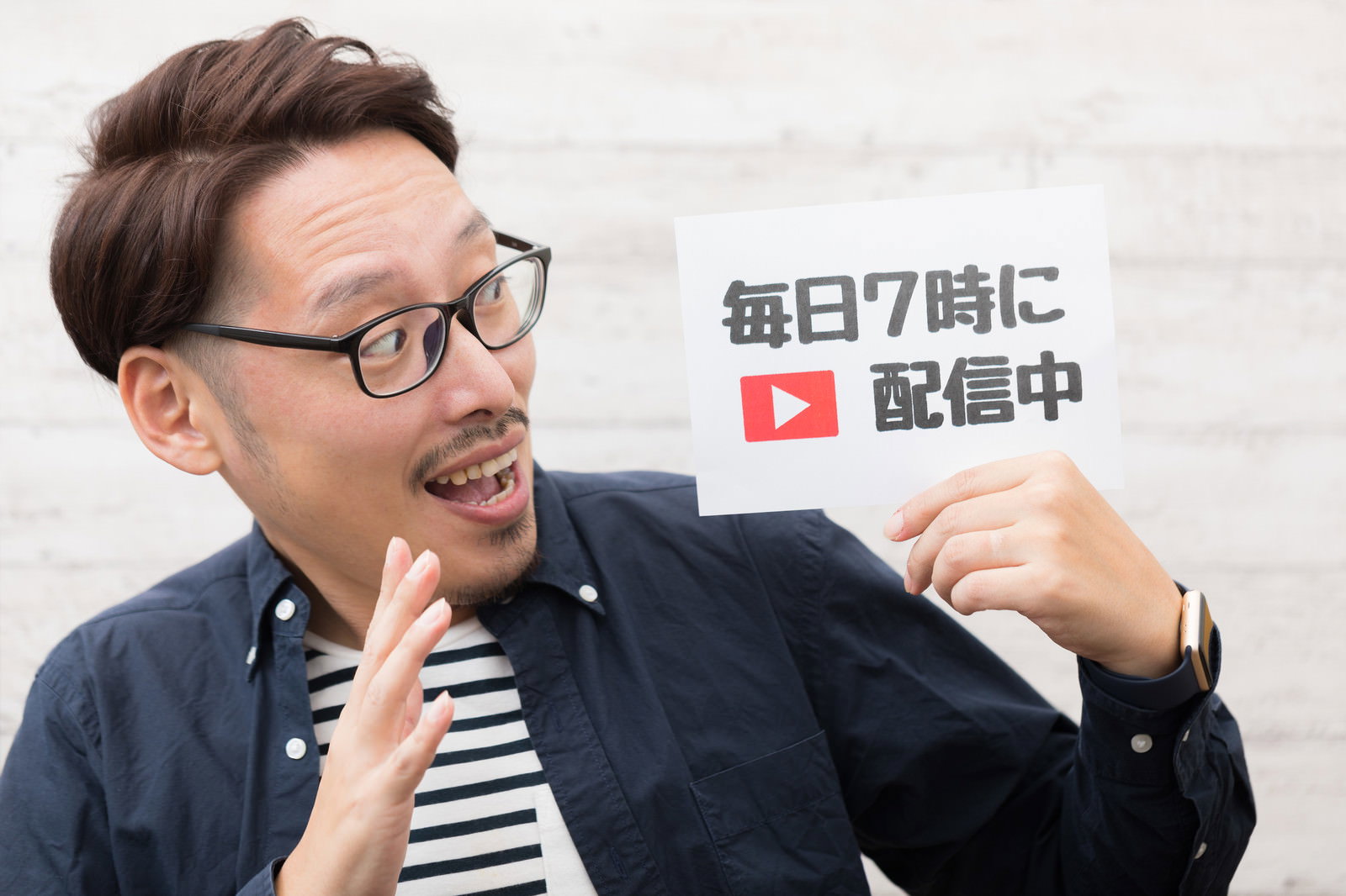 配信告知の紙を掲げる眼鏡の男性［モデル：ゆうせい］