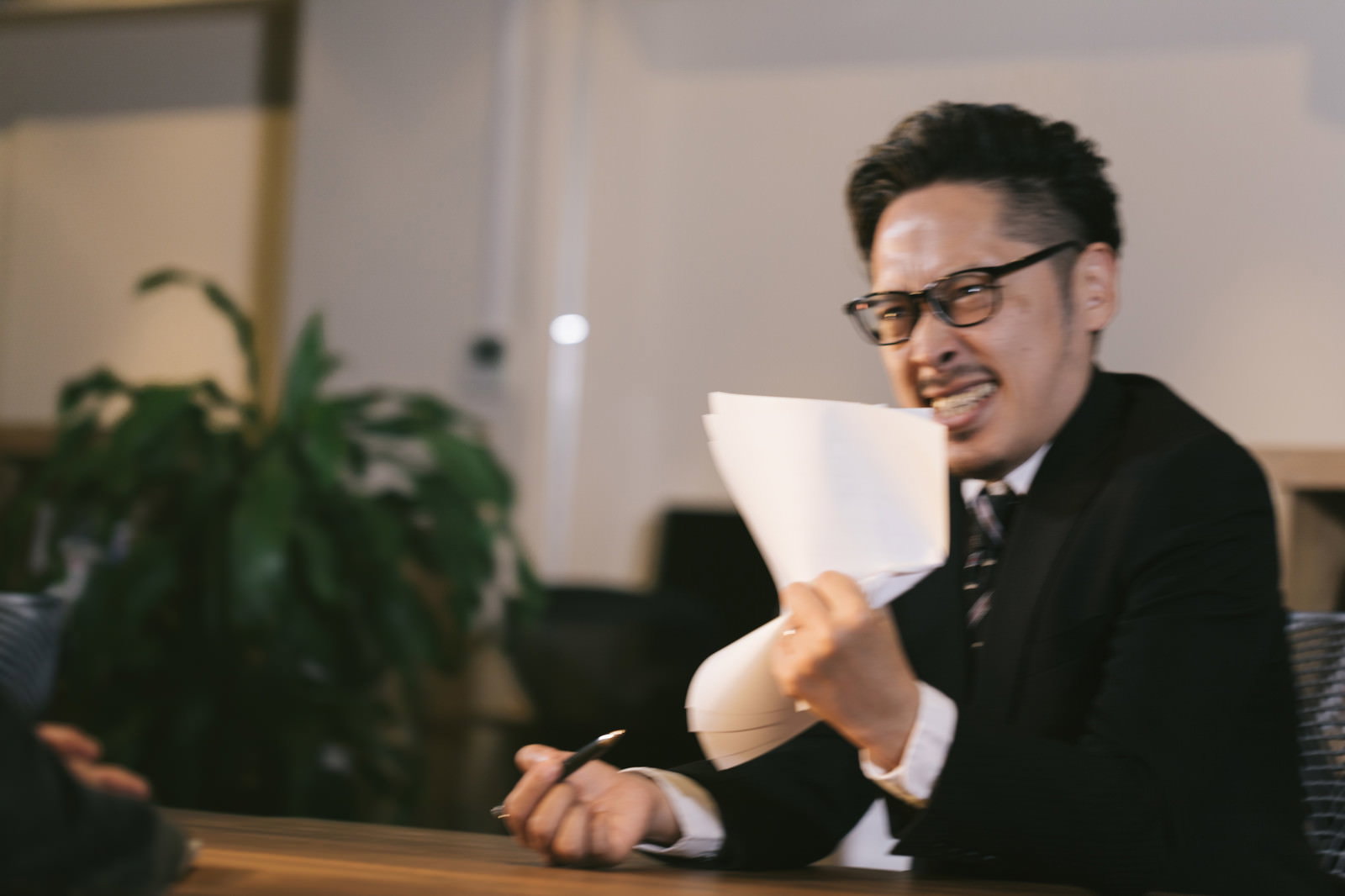 スーツの男性がデスク横で書類を握りつぶしながら激しく怒っている様子［モデル：ゆうせい］