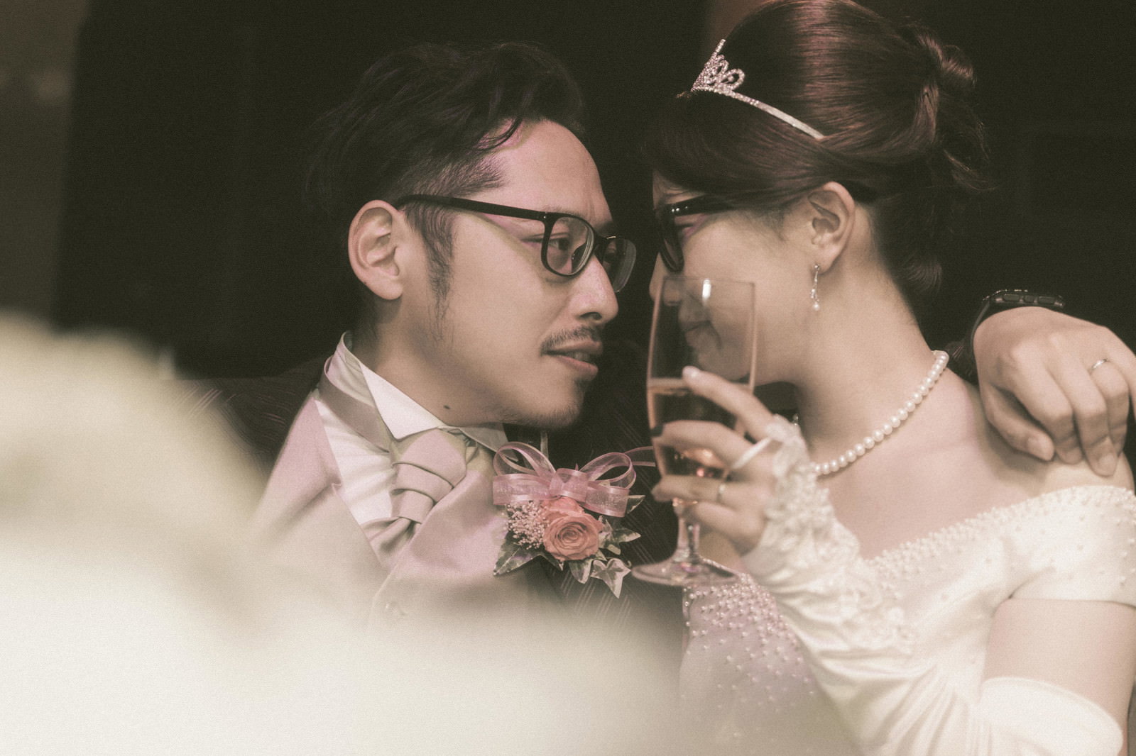 眼鏡の新郎がピンク色のネクタイについて語りかけ、真珠ネックレスの新婦が聞いている結婚式のシーン