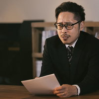 険しい表情で書類を持つ取引先の男性、スーツ姿で真剣な対応の写真