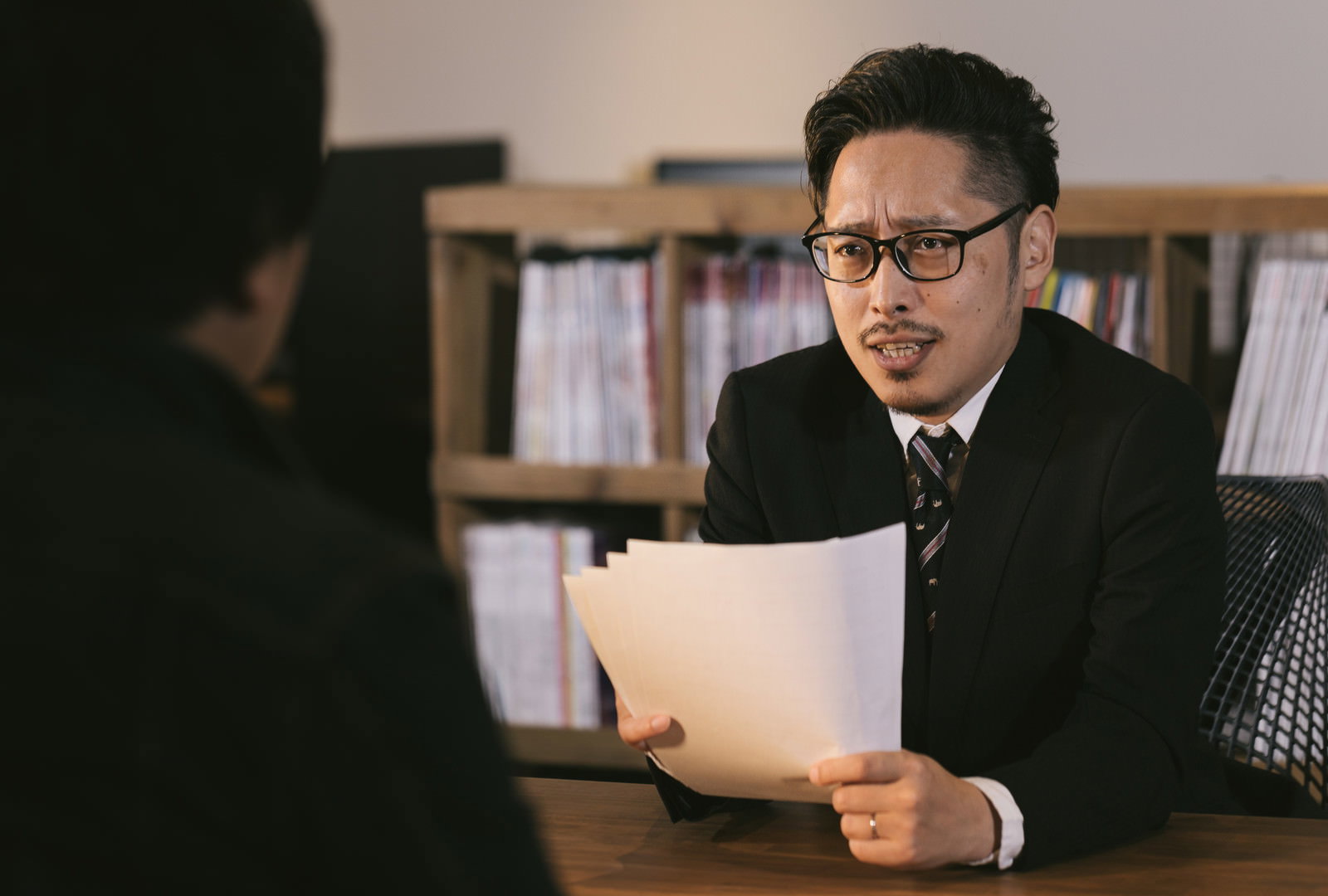 書類を手に食い入るような表情で説明するスーツ姿の男性［モデル：ゆうせい］