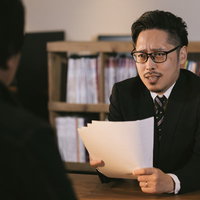 必死な形相で資料に食らいつく眼鏡をかけた営業マンの写真