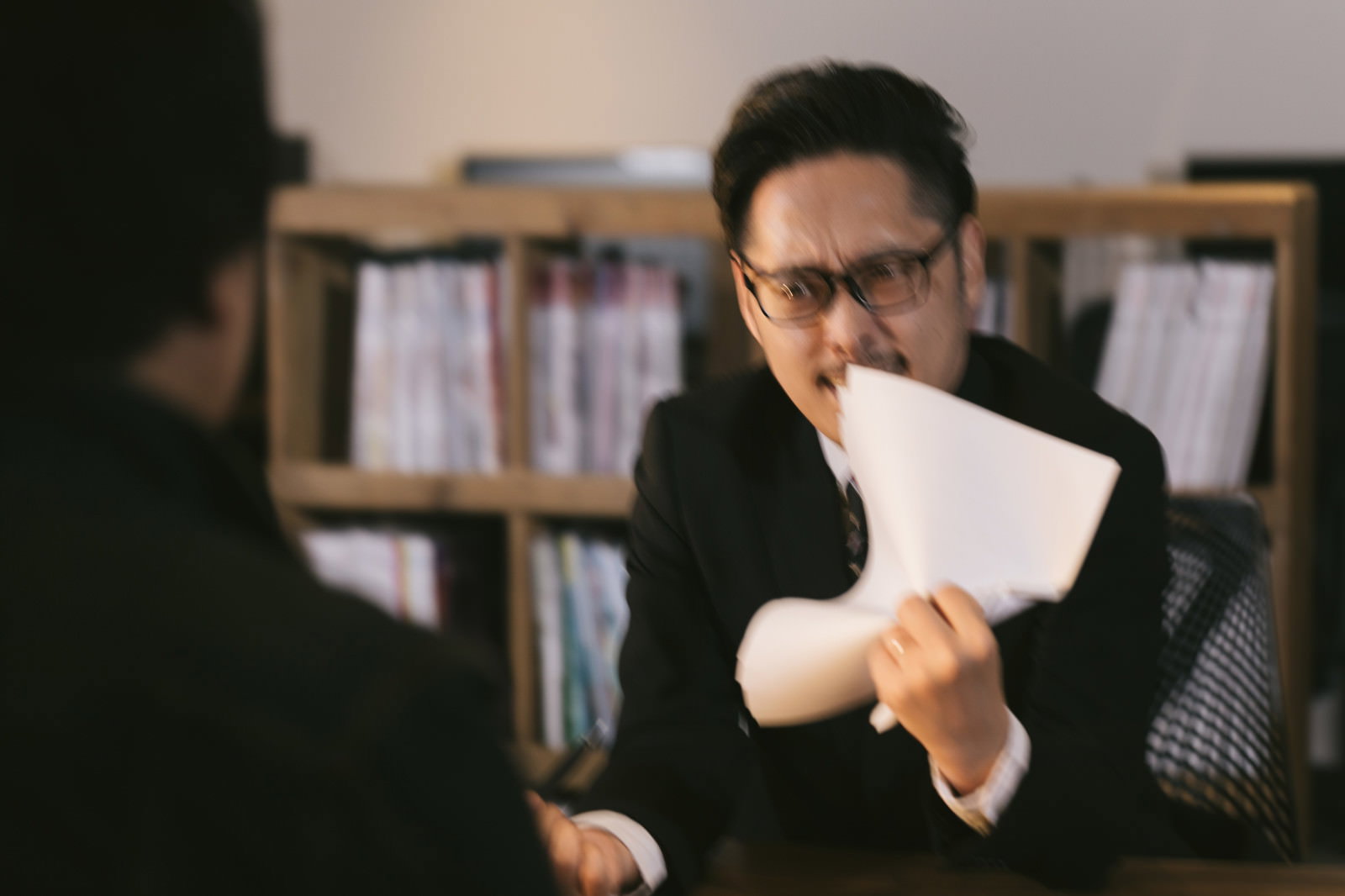 会議中に書類を握り潰す眼鏡の男性［モデル：ゆうせい］