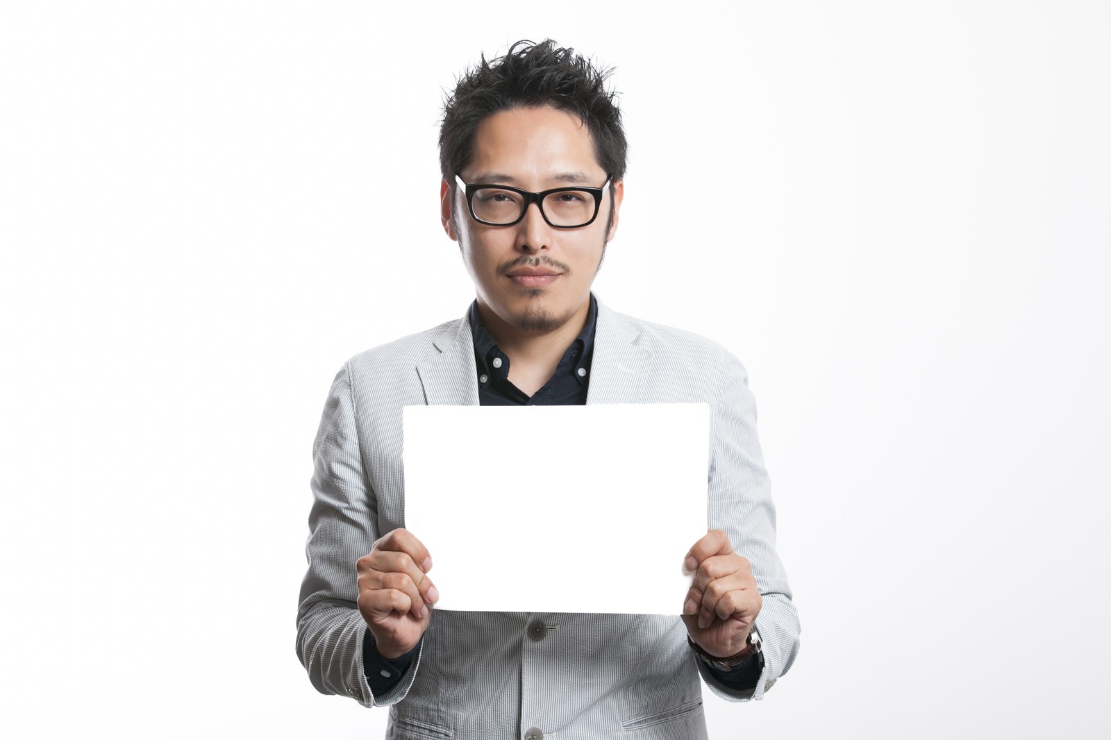 ホワイトボードを持つメガネの男性がカメラに向かって立つ［モデル：ゆうせい］