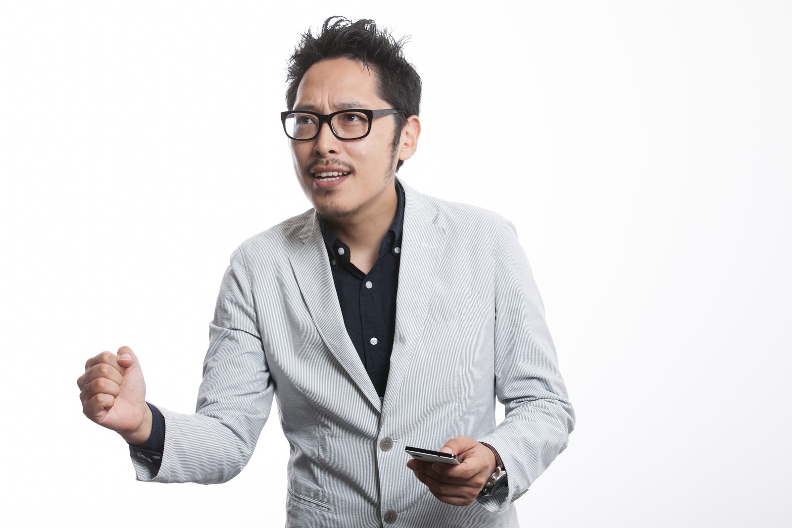 グレーストライプスーツを着た眼鏡の男性がスマートフォンを持ちながら身振りを交えてプレゼンする様子［モデル：ゆうせい］