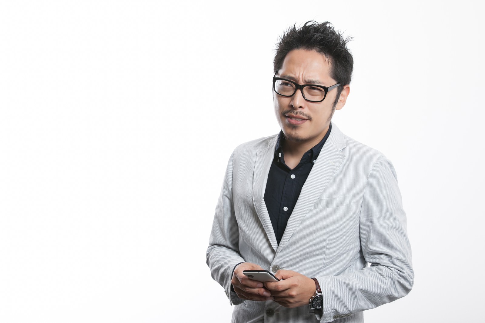 眼鏡をかけた男性がスマートフォンを持ち、落ち着かない様子で下を向いている［モデル：ゆうせい］