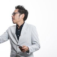 スマホを片手に熱く説明するグレーブレザーの男性社長の写真