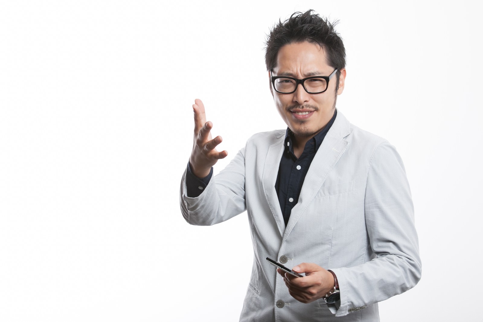 スマートフォンを持ちながら右手で身振りをする眼鏡をかけた社長男性［モデル：ゆうせい］