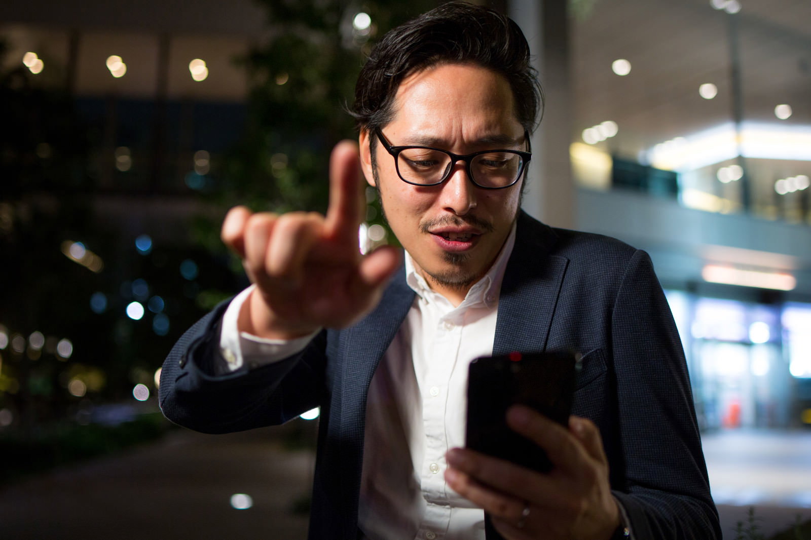 夜間にスマホで道案内する眼鏡のビジネスマン［モデル：ゆうせい］