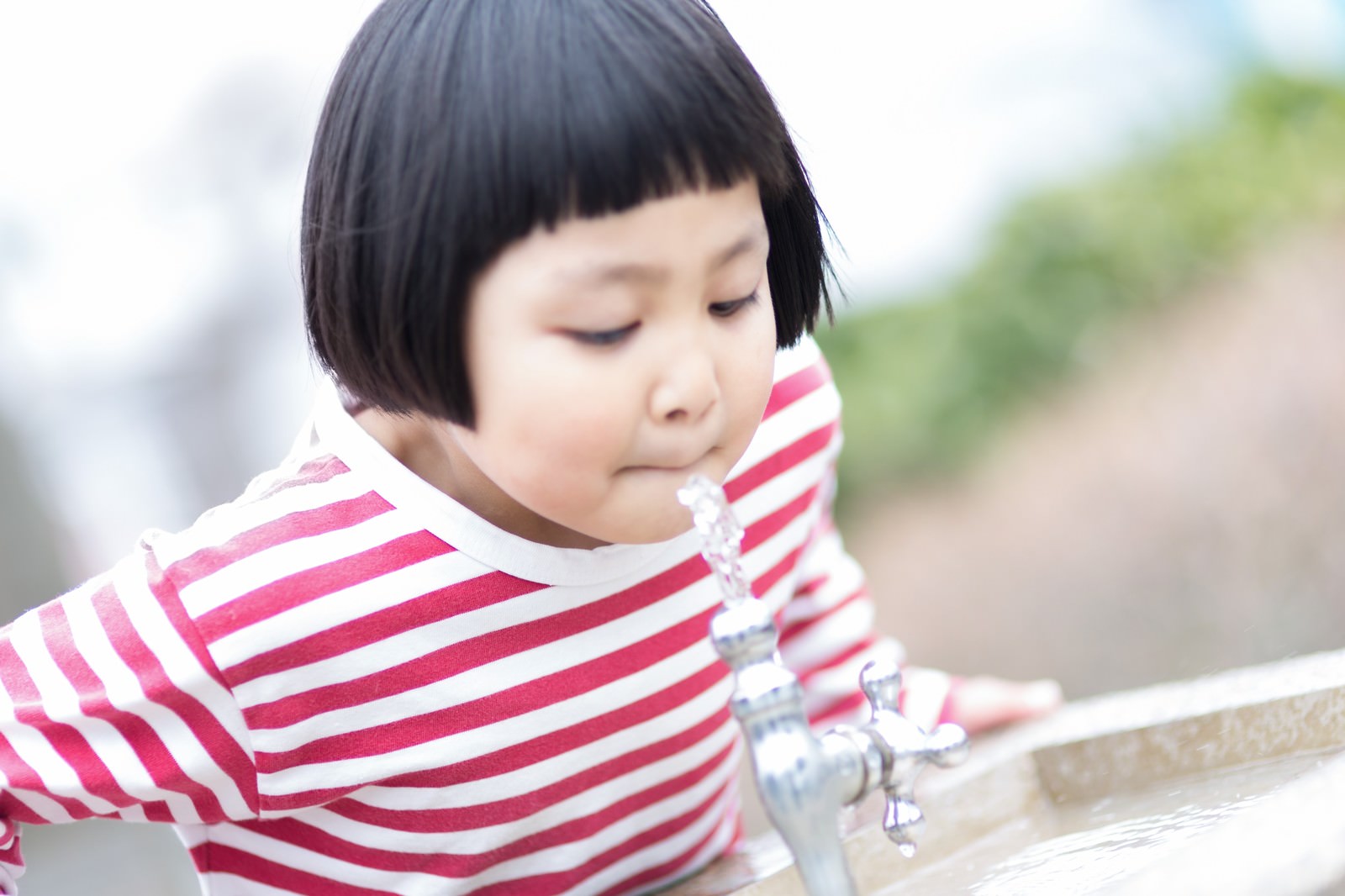 公園の水飲み場で水を飲む前髪パッツンの少女［モデル：ゆうき］