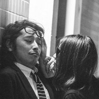 窓の光が入る室内で向き合うスーツの眼鏡男性と後ろ姿の長い髪の女性の写真