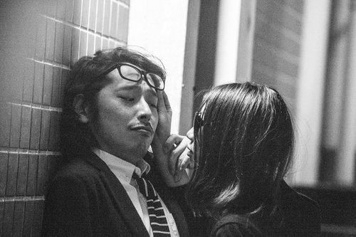 窓の光が入る室内で向き合うスーツの眼鏡男性と後ろ姿の長い髪の女性