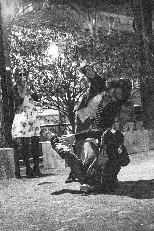 木のベンチに座る女性2名と地面にしゃがむ人物が屋外の明るい場所で写る写真