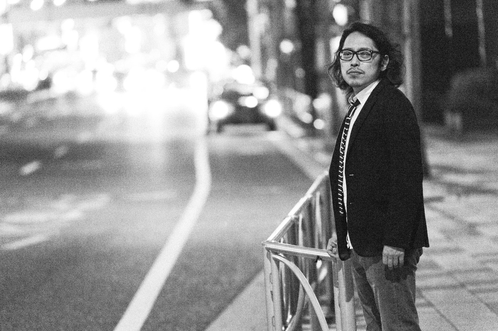 夜の街路に立つスーツ姿の男性［モデル：ゆうせい］
