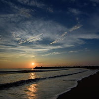 朝焼けの海岸に打ち寄せる波とレイラインの写真