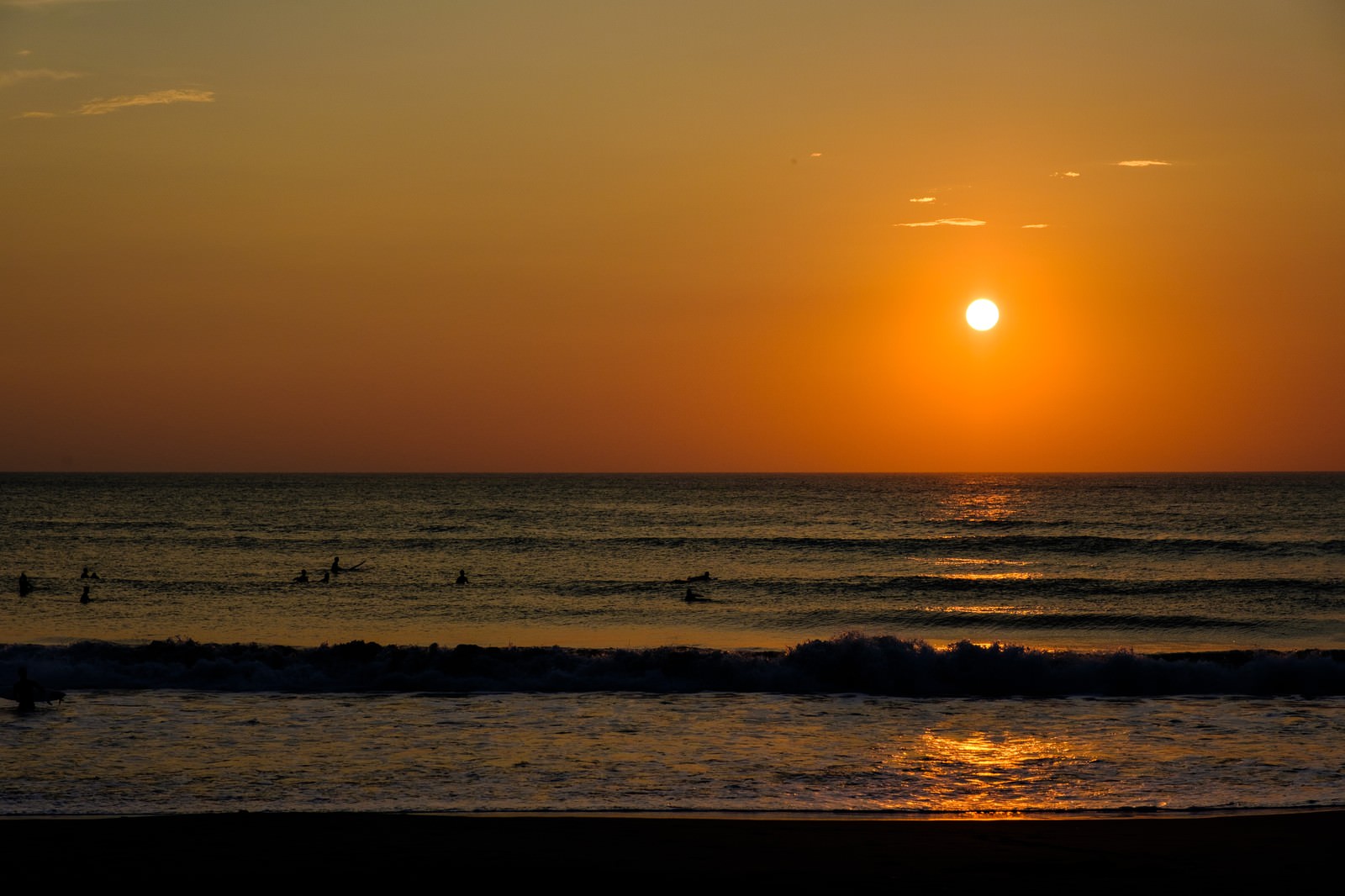 朝日に照らされた海で砕ける波のシルエット、オレンジ色の空と太陽が輝く海面