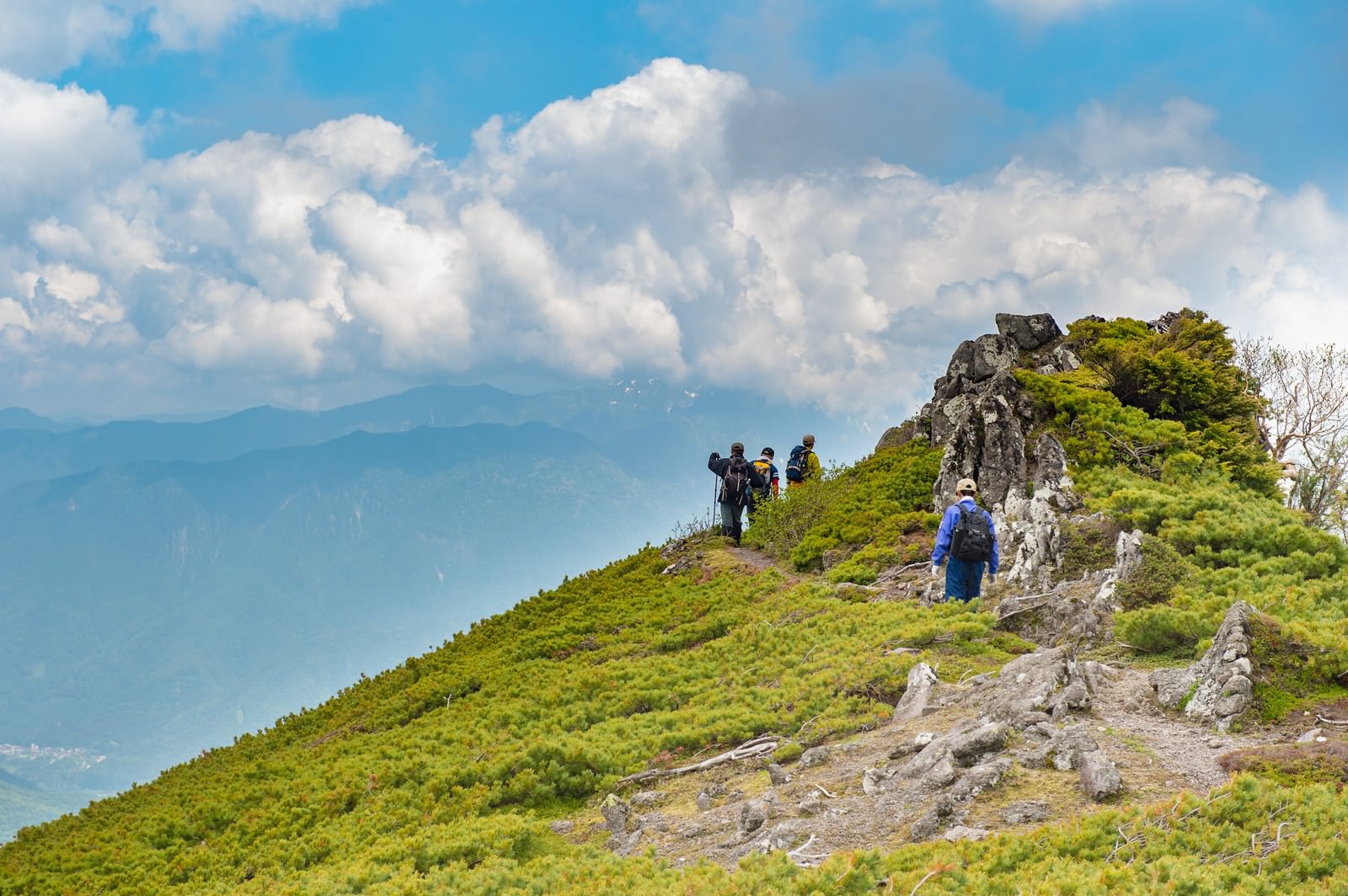 青空と白い雲の下、乗鞍新登山道の稜線を歩く登山者たち