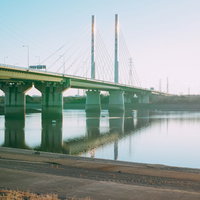 陽が差し込む河川敷の橋と堤防沿いの風景の写真