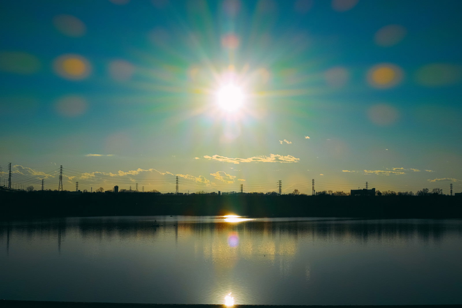 夕焼けの空と太陽の光が水面に反射する河川敷の風景