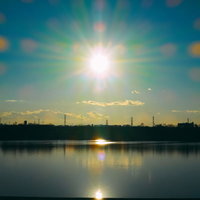 夕暮れの河川敷で太陽の光が水面に反射する風景の写真
