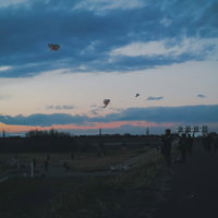 夕暮れの河川敷で凧上げする家族連れの人たちの写真