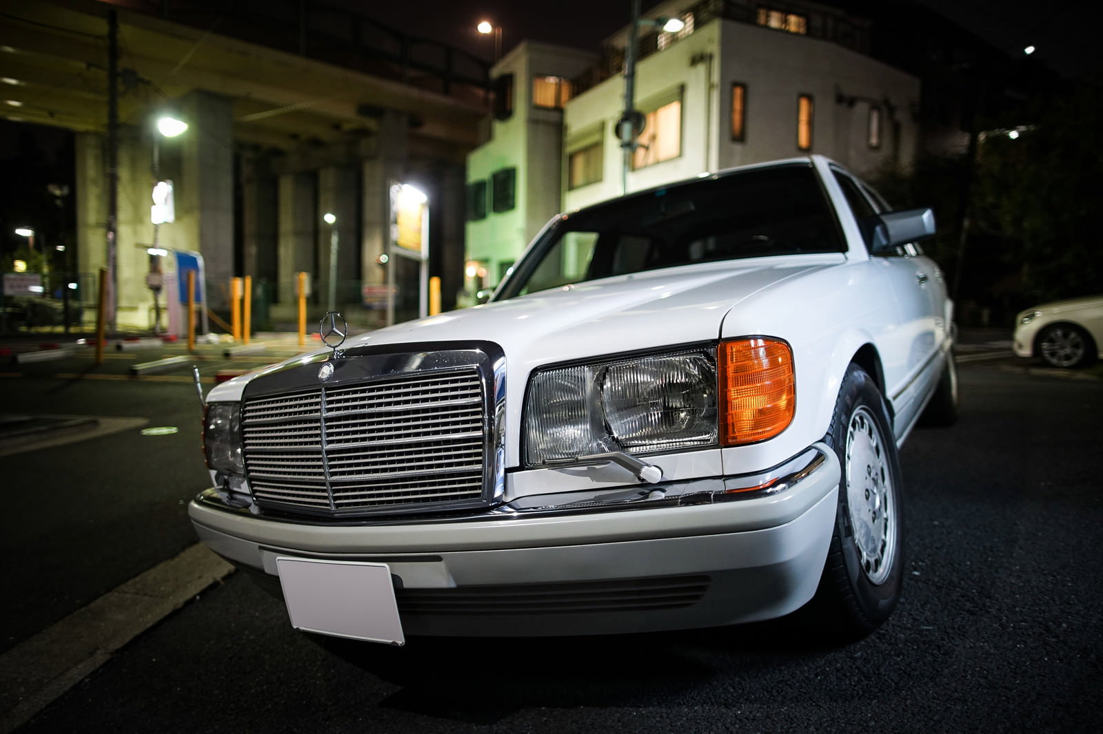 夜の街並みに駐車している白い旧型メルセデスベンツの正面