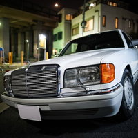 夜の街並みに駐車する白い旧型メルセデスベンツの写真