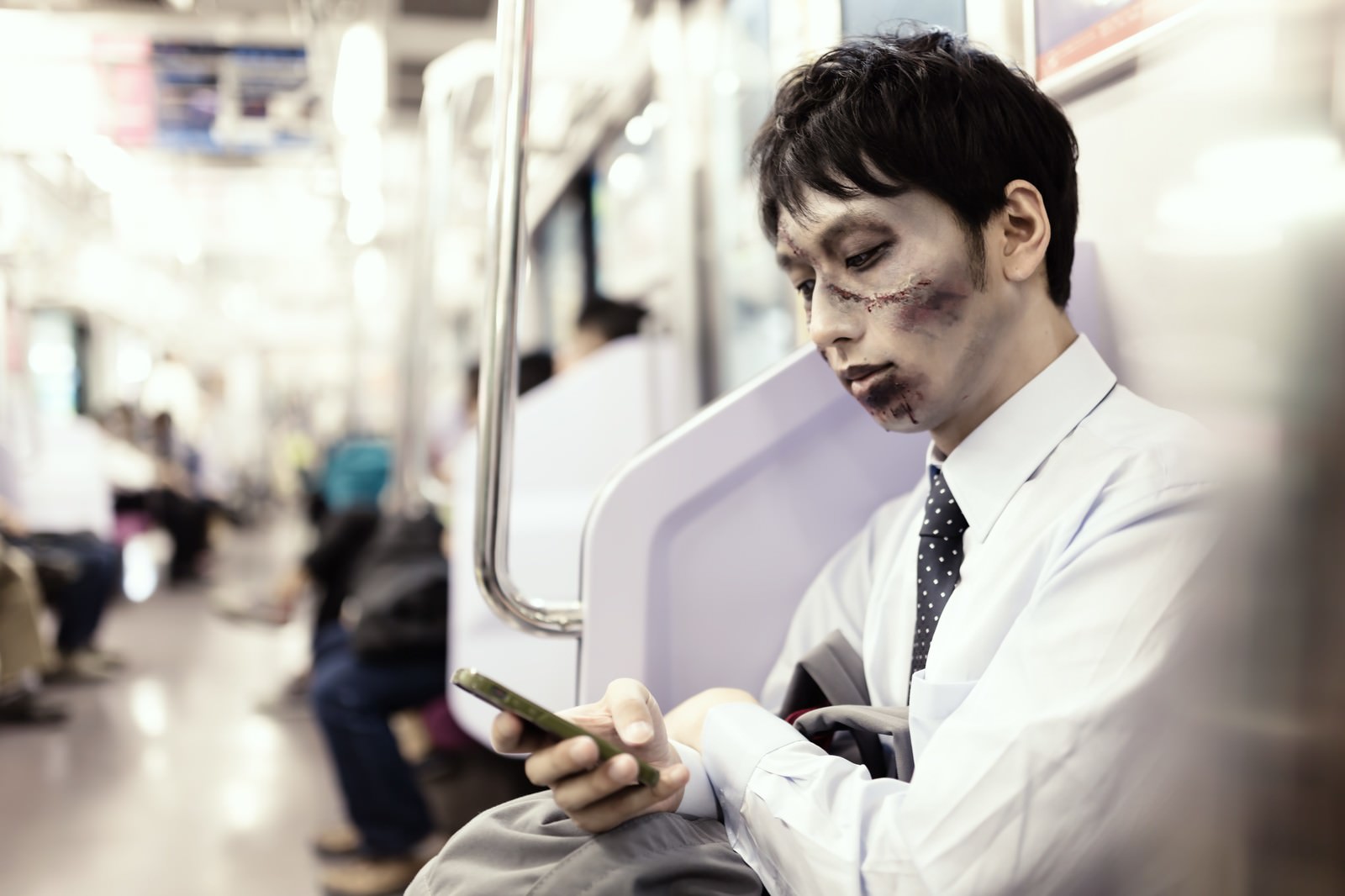 電車内でスマホをチェックするゾンビメイクの通勤男性［モデル：大川竜弥］