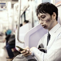 電車内でスマホをチェックするゾンビメイクの通勤男性の写真