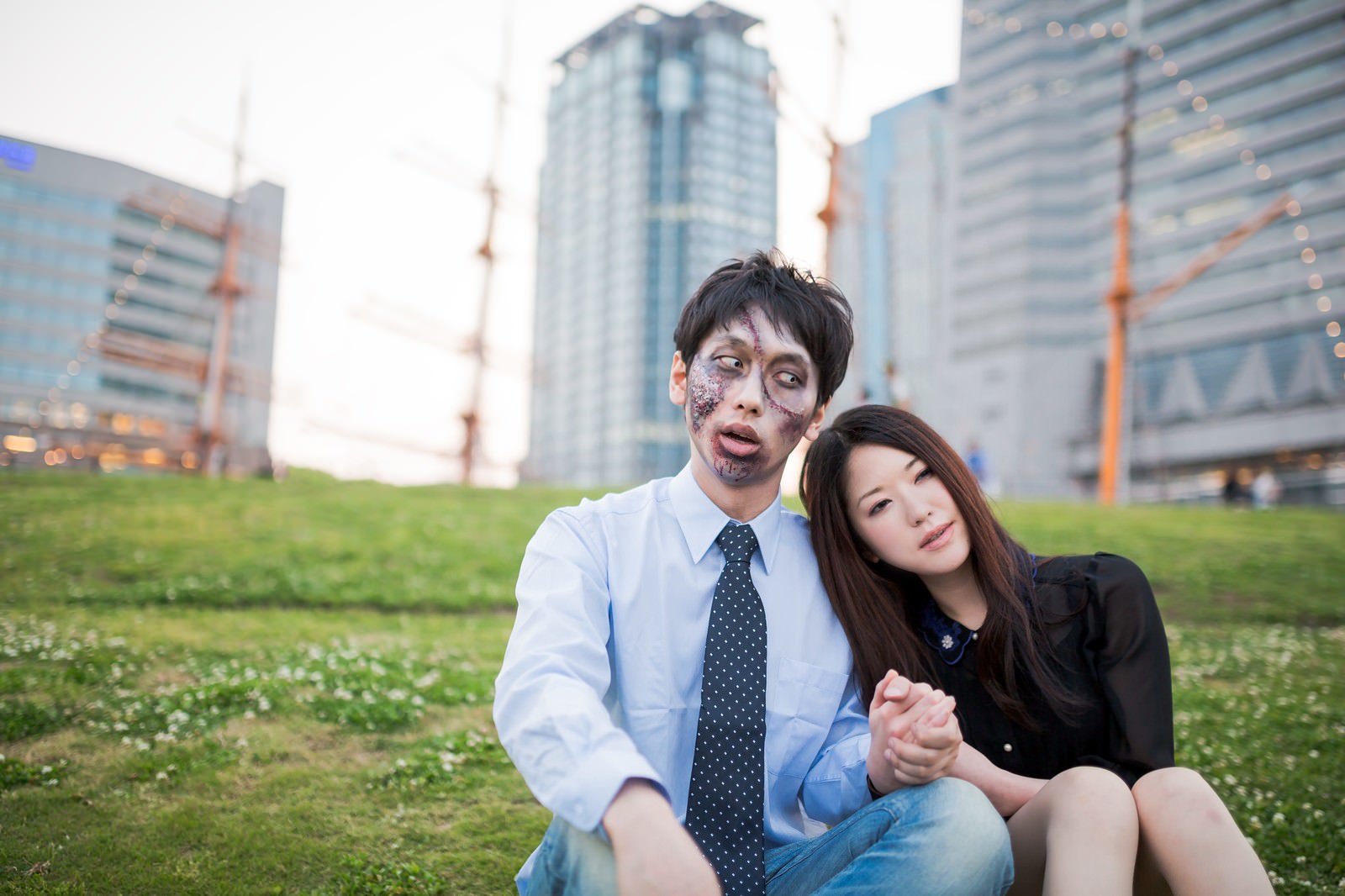 ビルを背景に、腐乱メイクの青シャツ男性が口を開けて女性に話しかけ、女性は横を向いて聞いている［モデル：大川竜弥 シマヅ］
