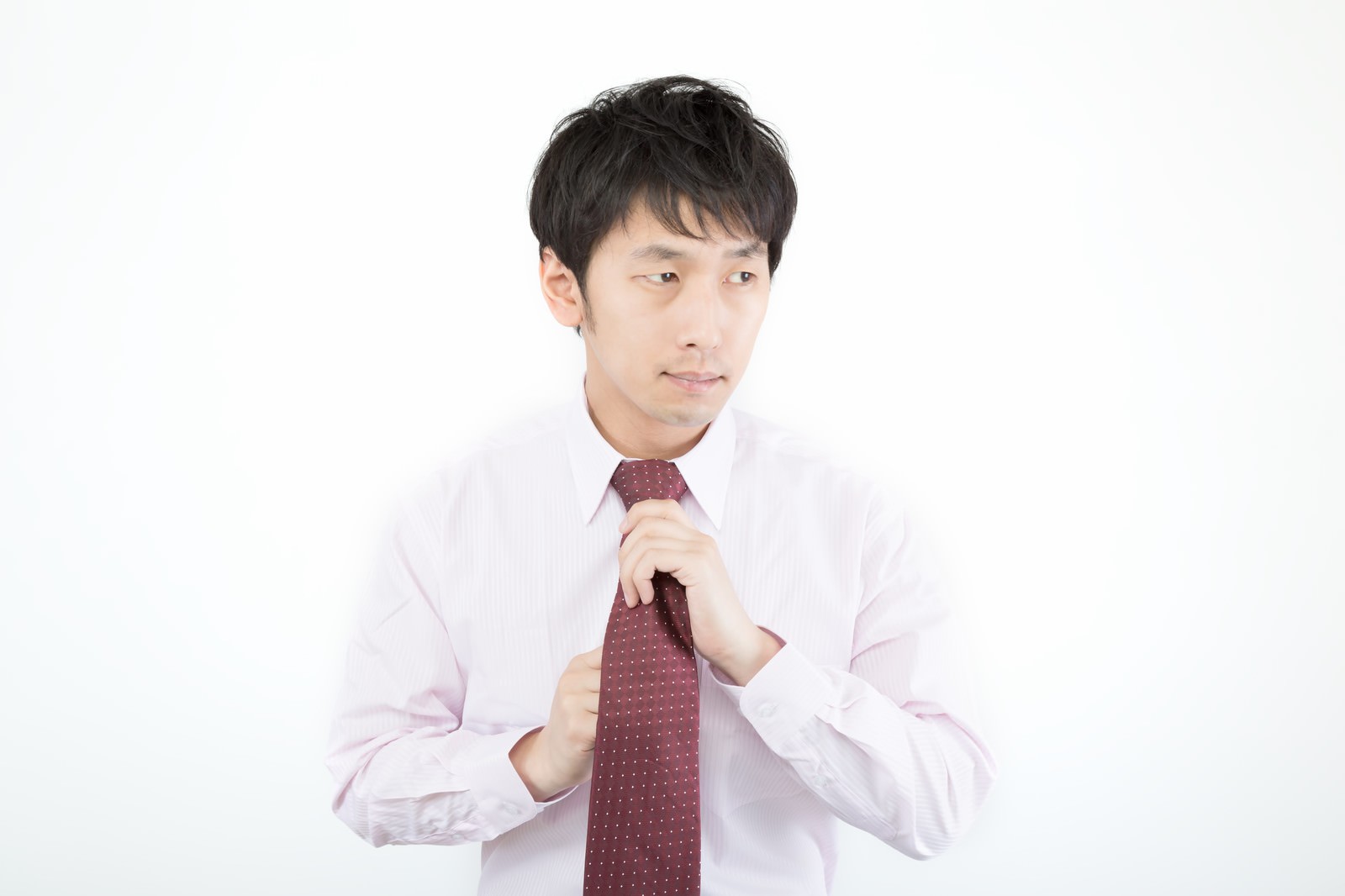 白背景でネクタイを締め直す男性［モデル：大川竜弥］