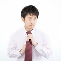 白背景でネクタイを締め直すピンクシャツの新入社員の写真