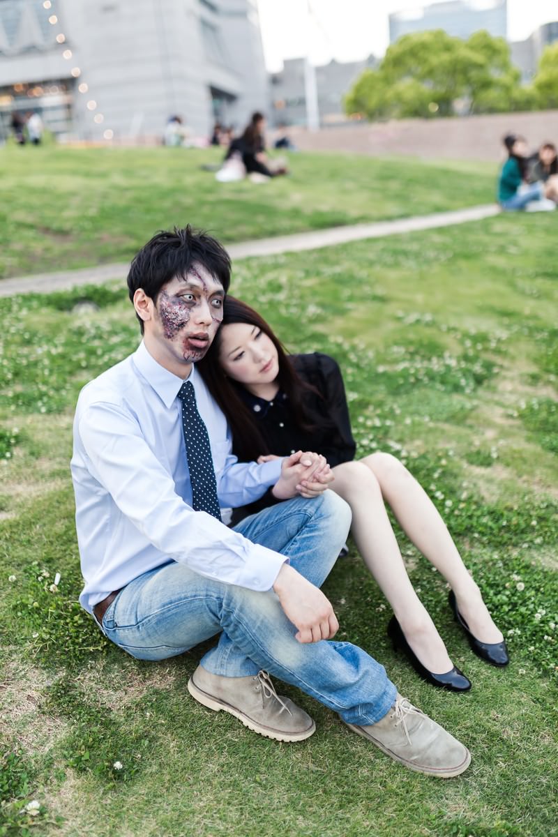 ゾンビメイクのカップルが芝生に座って手をつなぐ［モデル：大川竜弥 シマヅ］