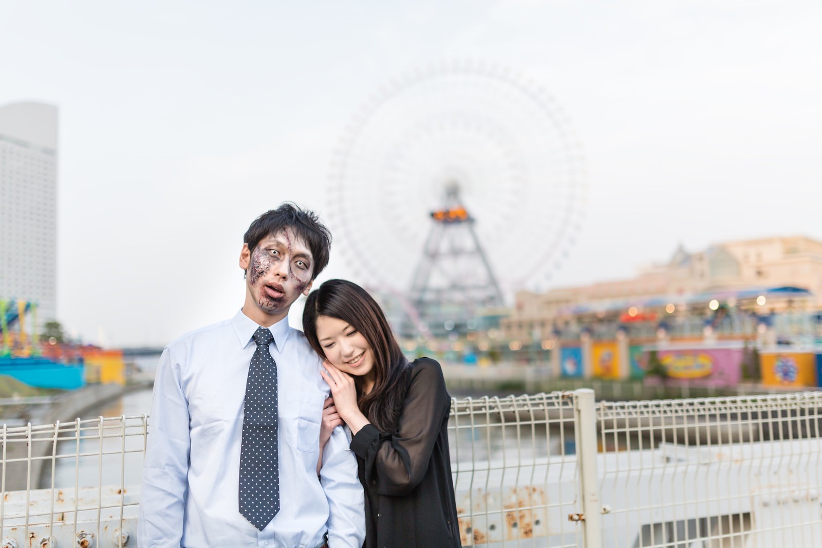 遊園地で並んで立つゾンビメイク男性と黒い服の女性［モデル：大川竜弥 シマヅ］