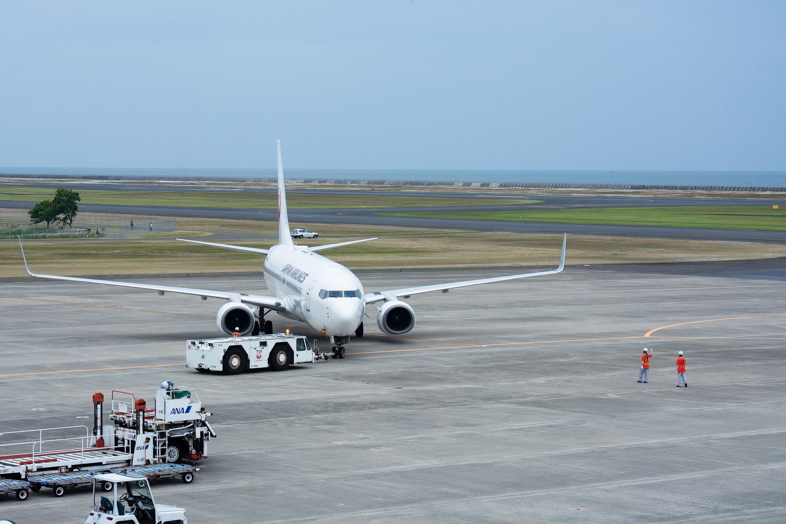 トーイングカーで押し出される日本航空の旅客機と誘導するグランドハンドラー
